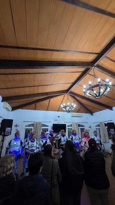 Grupo de personas actuando en un evento dentro de un salón con techos altos y candelabros.