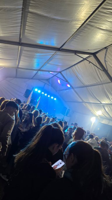 Multitud en un evento dentro de una carpa, con luces azules y niebla.