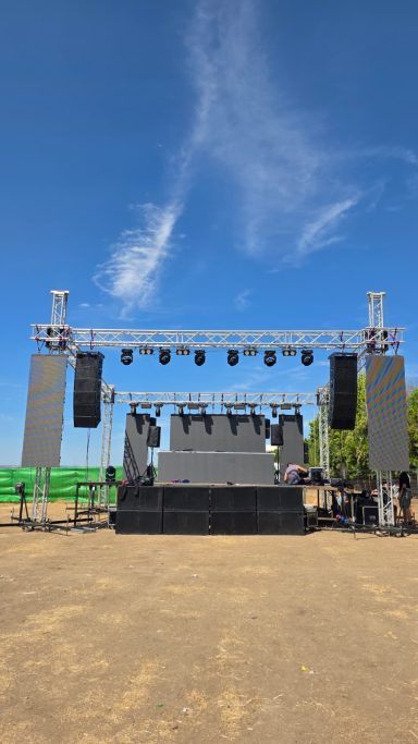 Escenario grande con altavoces, preparado para un evento al aire libre bajo un cielo azul.