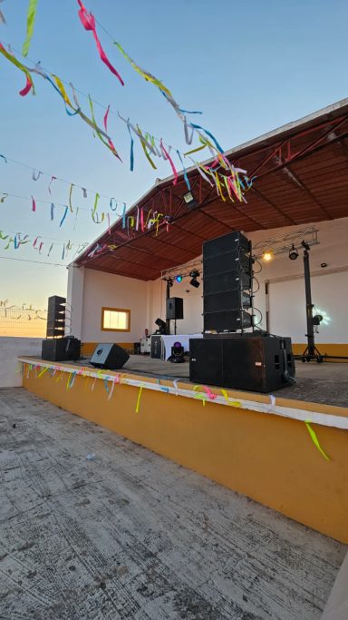 Escenario preparado para un evento al aire libre con altavoces y decoraciones de colores.