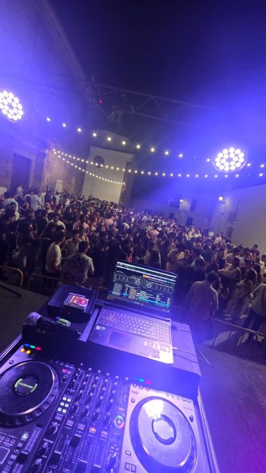 Una multitud en un evento nocturno, vista desde una mesa de DJ iluminada.