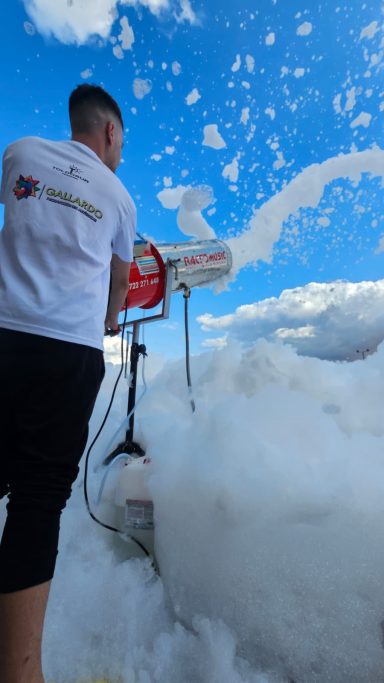 Persona usando una máquina de espuma bajo un cielo azul con nubes.